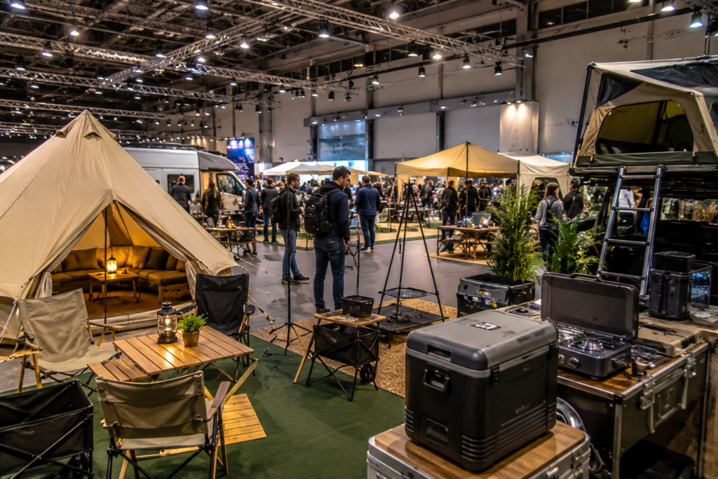 Verschiedene moderne Camping Setups auf einer großen Outdoor Ausstellung Messe mit Besuchern, Zelten, Campingmöbeln und Outdoor Zubehör
