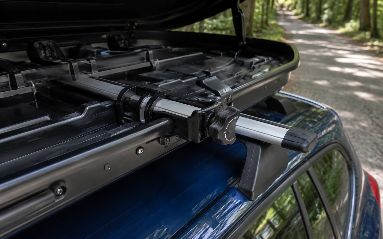Ein modernes Krallensystem fixiert eine geöffnete Dachbox auf den Schienen eines Autos