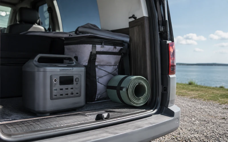 Powerstation steht im geöffneten Kofferraum eines Vans neben Campingausrüstung