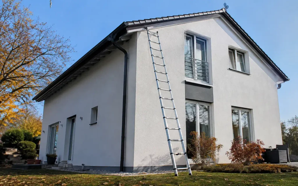 Ausgezogene Teleskopleiter an der Fassade eines zweistöckigen Hauses zur Dachrinnenreinigung